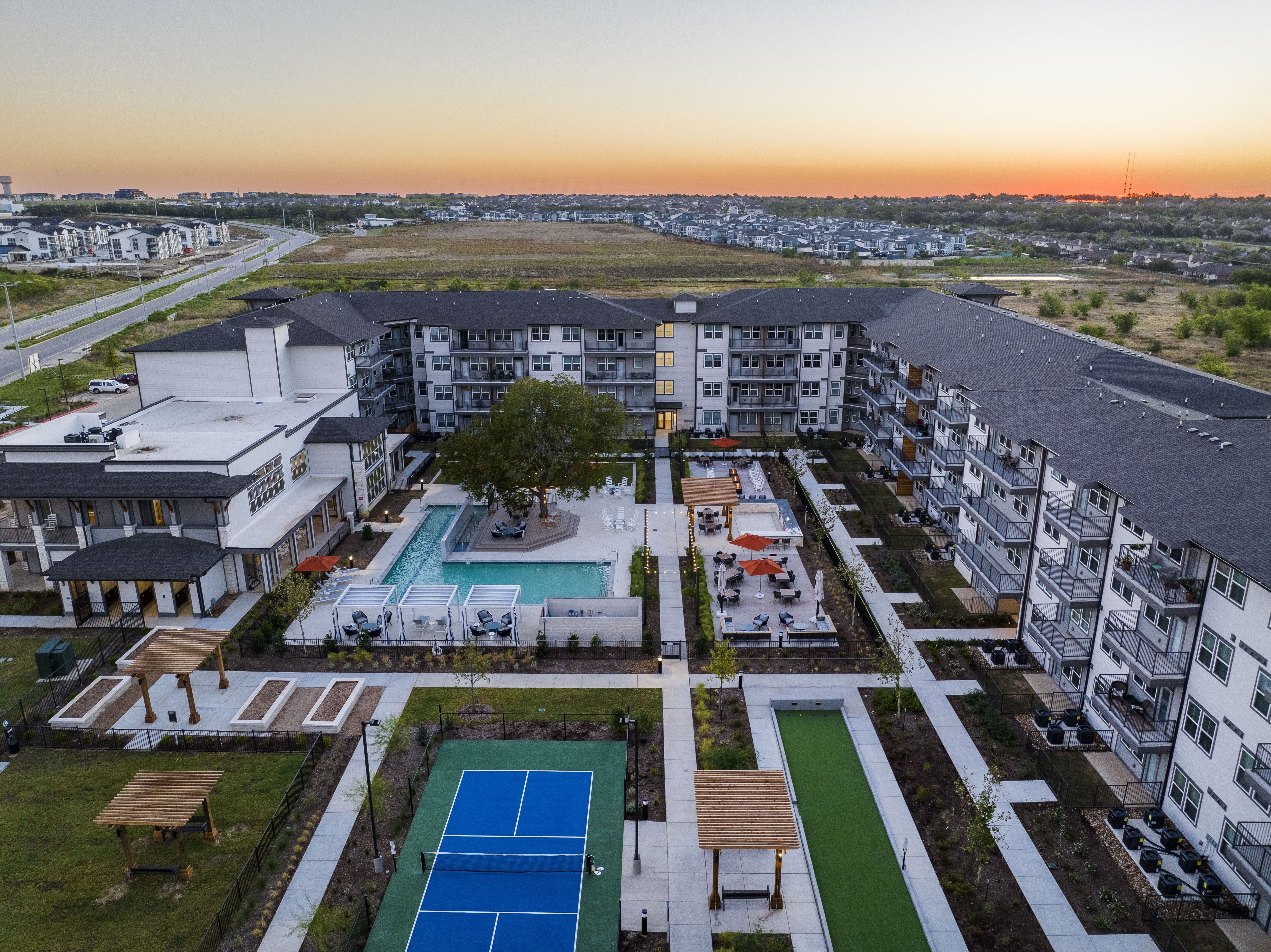 an aerial view of a resort-style pool, courtyard, pickleball courts, bocce ball and lawn at a senior apartment community